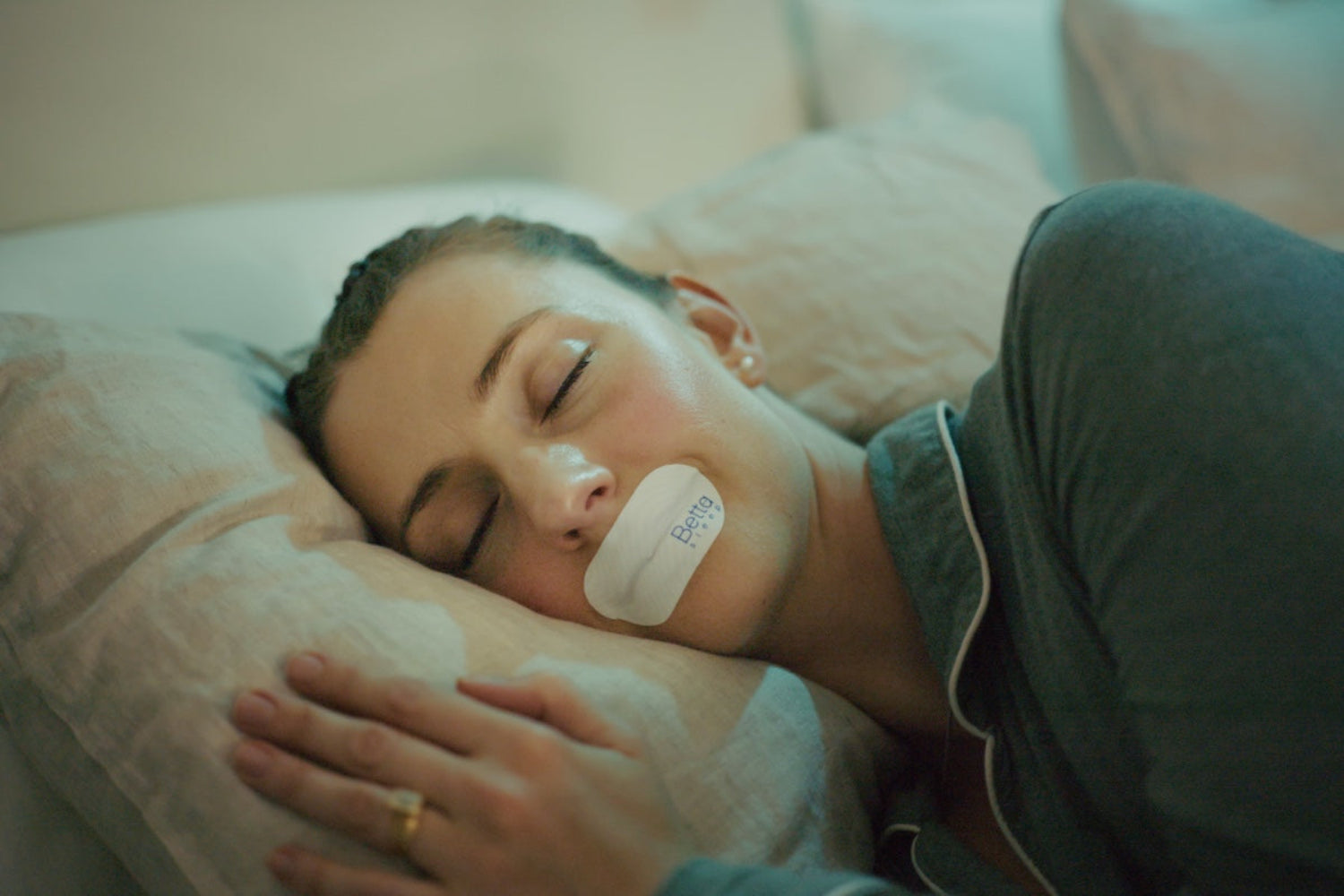 Woman lying in bed with Betta Sleep Collagen-Infused Mouth Tape on her mouth